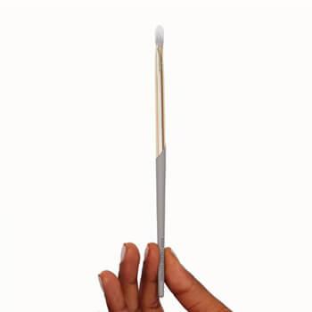 An image of a COMPLEX CULTURE eye makeup brush held upright by two fingers Mobile
