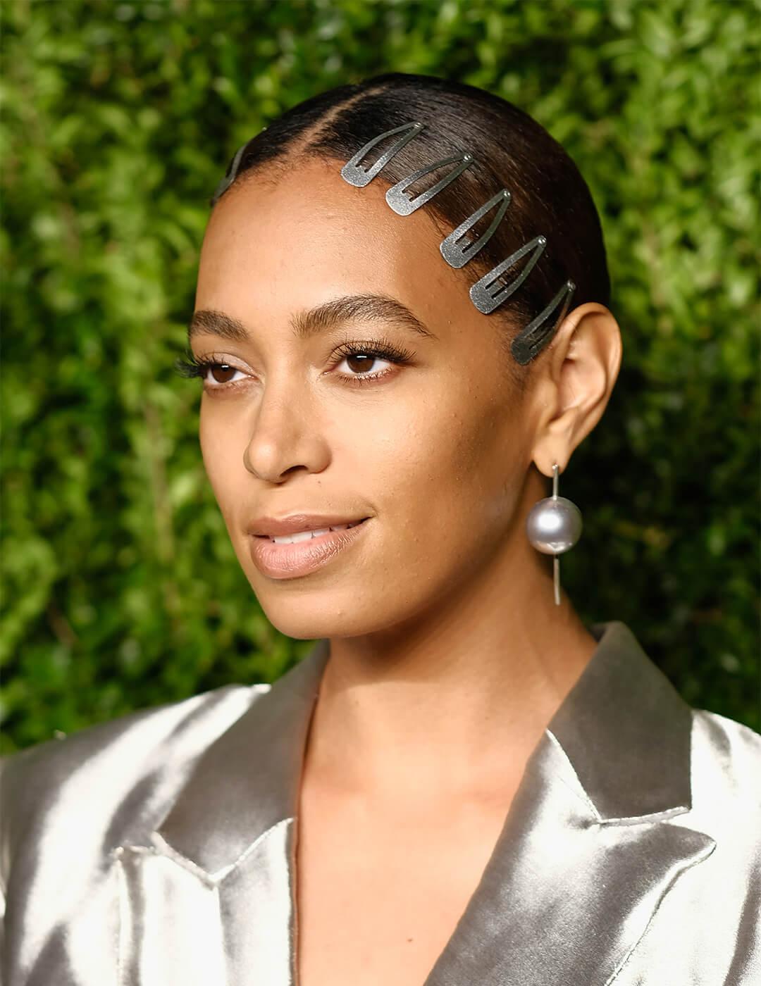 Solange Knowles in a silver suit rocking a slicked back hair style embellished with 5 hair clips Mobile