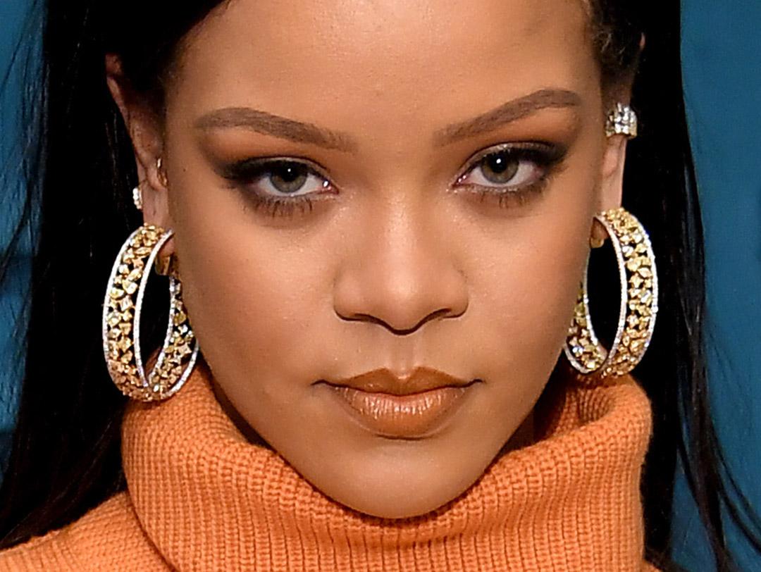 A photo of Rihanna looking fierce wearing an orange turtle neck, bejeweled gold hoop earrings with smoky eyes and a nude lip color Desktop