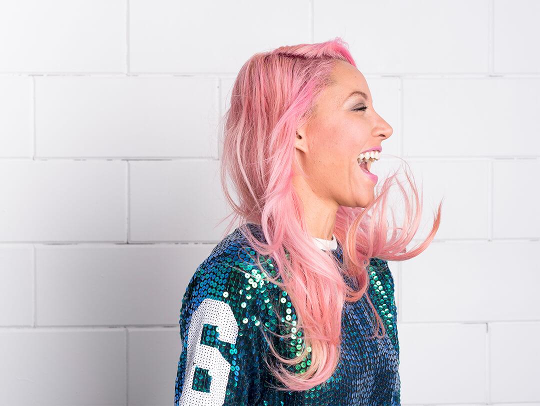 Profile image of a woman with pink hair and wearing a sequined top smiling with mouth wide open Desktop