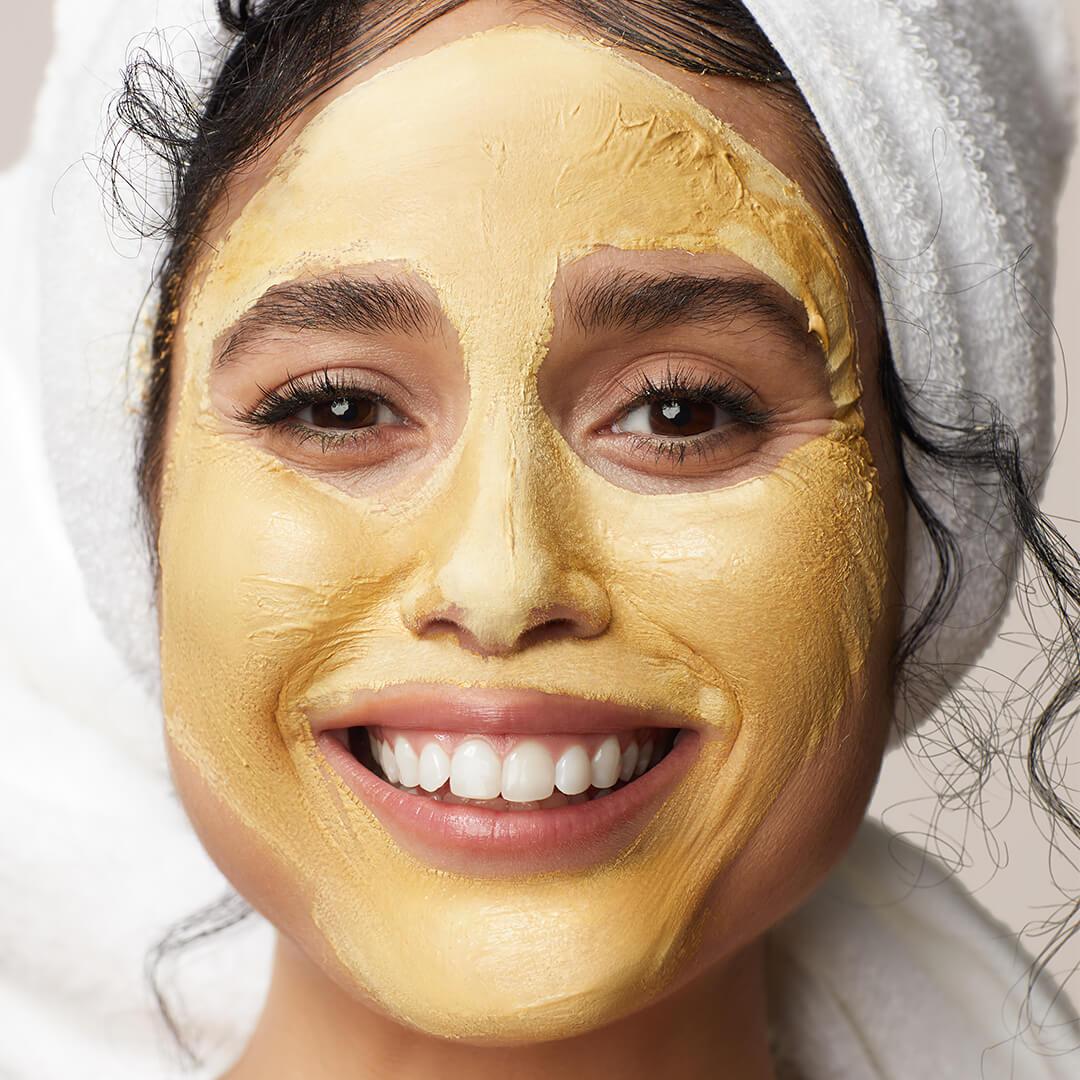 Close-up of a smiling model with gold mud mask on her face Desktop